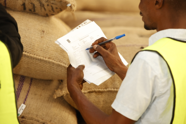 Un homme en gilet jaune note des informations sur un formulaire devant des sacs de jute.