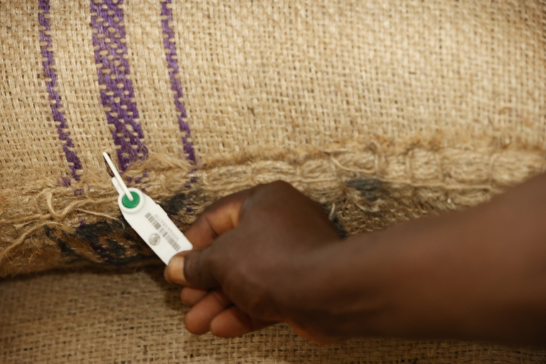 Une main noire attache une étiquette blanche avec un code-barres à un sac en toile de jute.