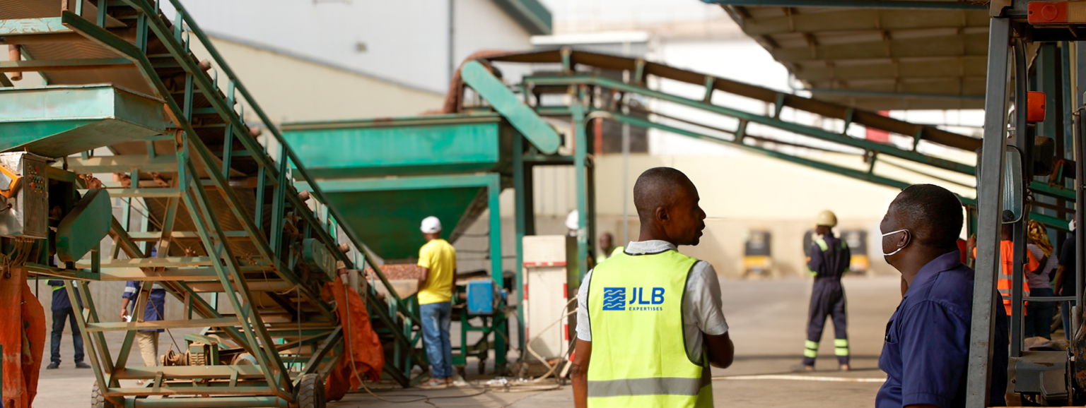 Des ouvriers discutent dans une usine avec des convoyeurs industriels en arrière-plan.