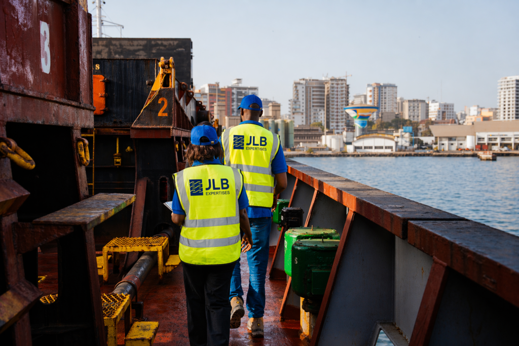 Deux agents de maintenance en gilets jaunes JLB Expertises marchent sur le pont d'un navire dans un port.
