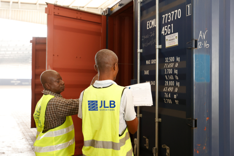 Deux hommes en gilets de sécurité jaunes inspectent un conteneur de transport maritime bleu.