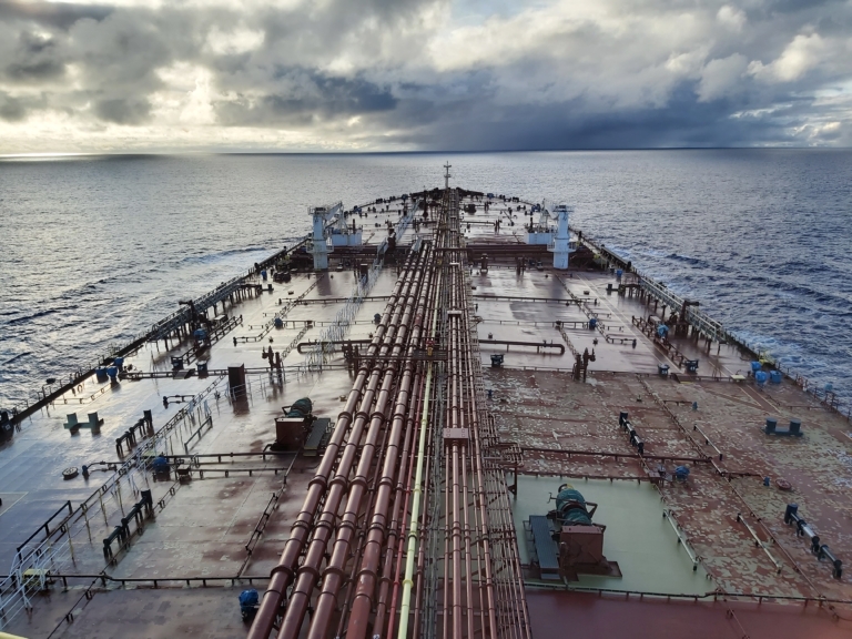 Vue plongeante du pont d'un pétrolier avec ses tuyauteries rouges s'étendant vers l'horizon sous un ciel nuageux.