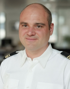 Portrait d'un homme chauve en uniforme blanc de pilote avec des épaulettes noires.