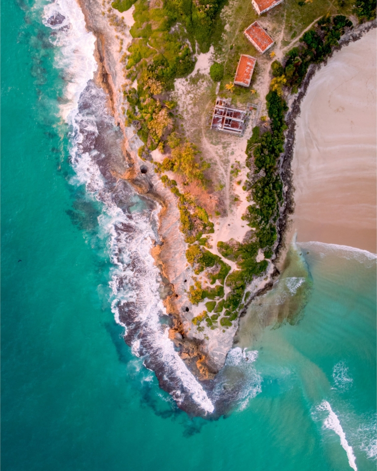 Vue aérienne d'une côte rocheuse escarpée bordée d'eaux turquoise et de quelques maisons isolées.