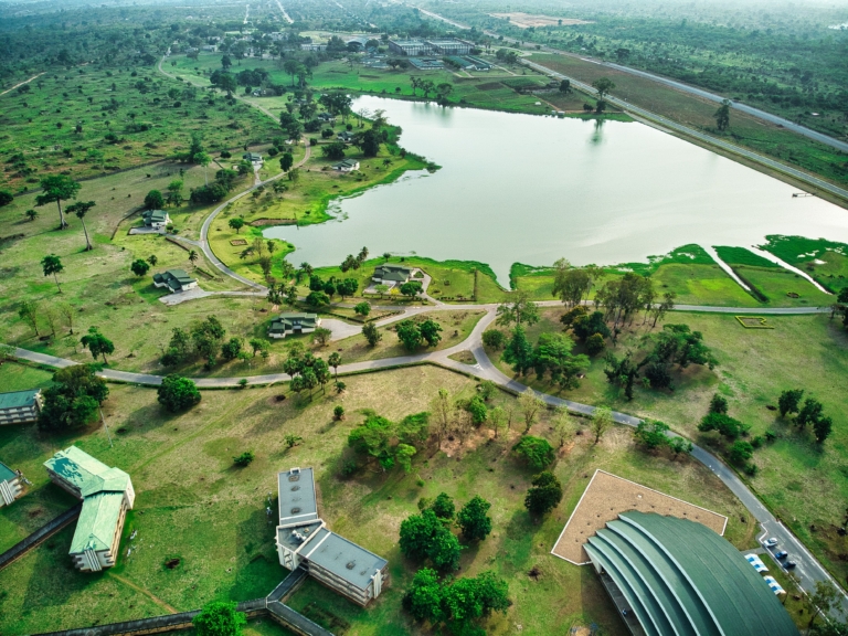 Vue aérienne d'un campus verdoyant avec un grand étang, des bâtiments dispersés et des routes sinueuses.