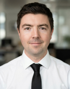 Portrait d'un homme aux cheveux bruns portant une chemise blanche et une cravate noire.
