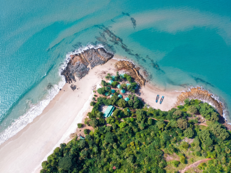 Vue aérienne d'une plage de sable blanc bordée d'une forêt tropicale et d'eaux turquoise cristallines.