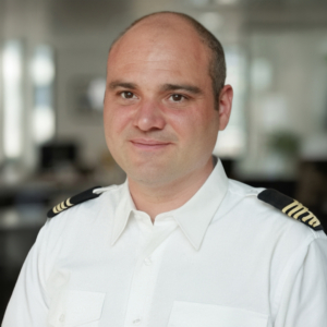 Portrait d'un homme chauve en uniforme blanc de pilote avec des galons dorés sur les épaules.